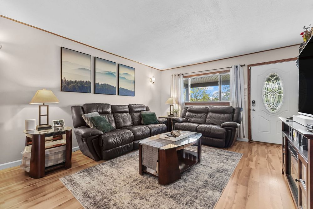 Bright living room featuring dark leather recliner sofa, hardwood floors, and front entry door.