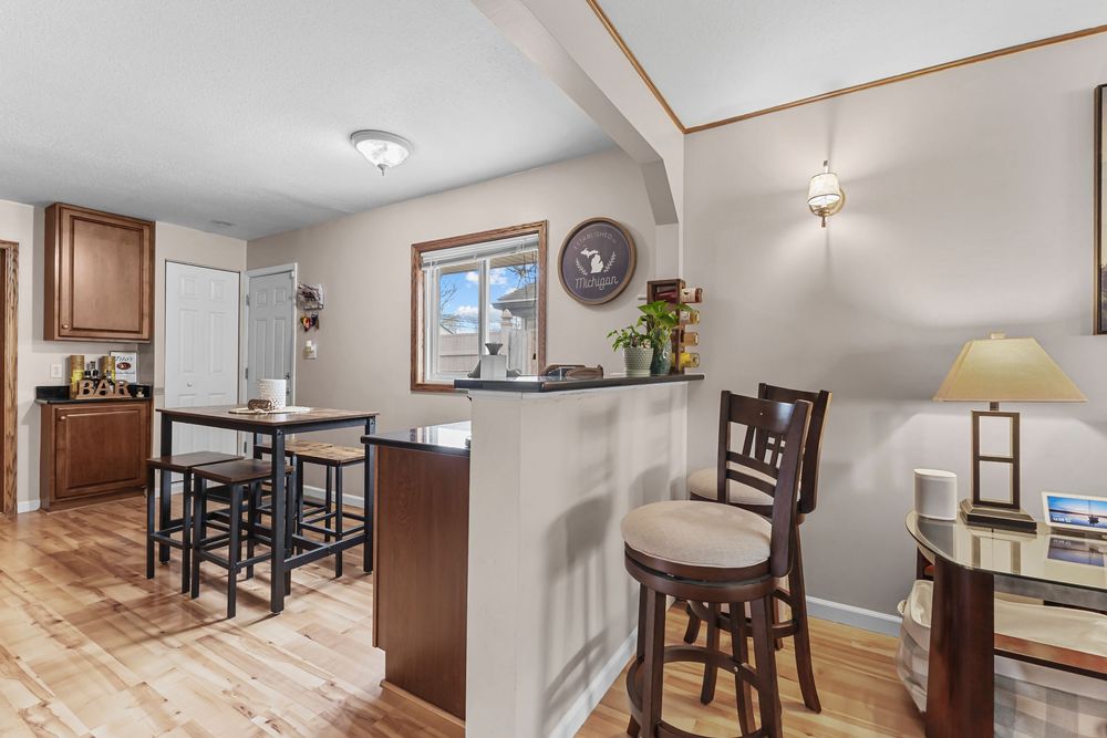 Open kitchen area with breakfast bar, bar stools, wood cabinets, and hardwood flooring.
