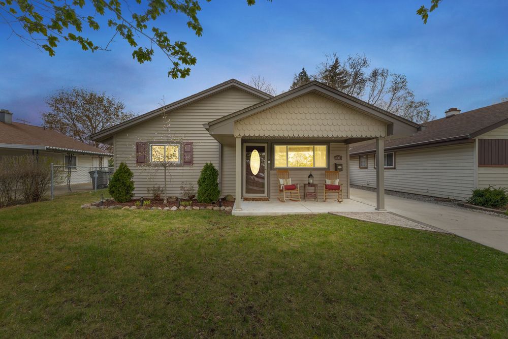 Cozy ranch-style home with covered front porch, rocking chairs, and well-maintained lawn photographed at dusk.