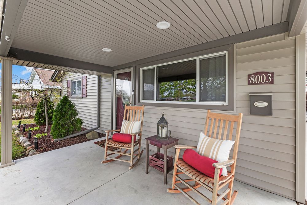 Inviting covered front porch with two rocking chairs and red cushions beside house number 8003.