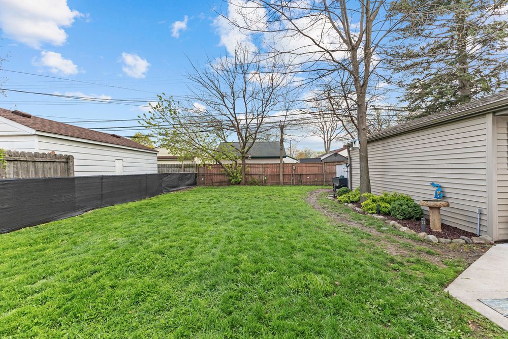 Spacious fenced backyard with lush green lawn, privacy fence, and detached garage structure.