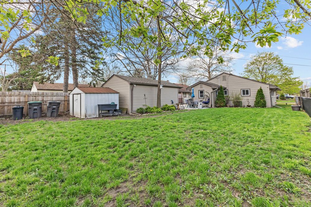 Large backyard with green lawn, storage shed, detached garage, and mature trees surrounding the property.