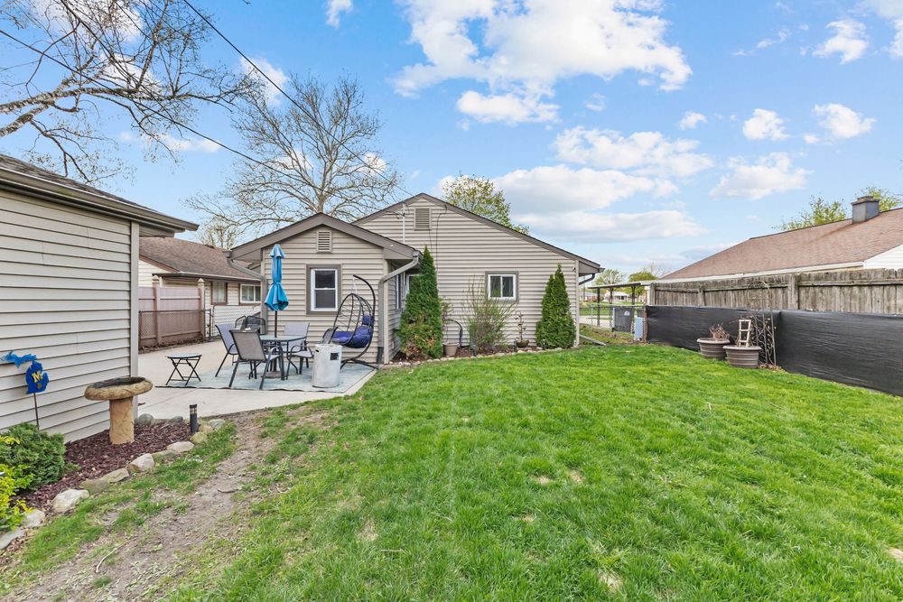 Backyard patio area with outdoor seating, fire pit, lush green lawn, and privacy fence surrounding the yard.