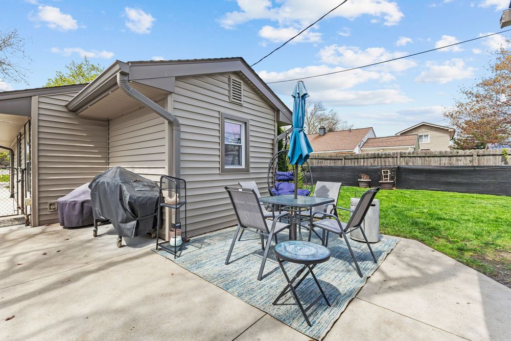 Cozy backyard patio with outdoor dining set, umbrella, and BBQ grill beside a beige sided home.