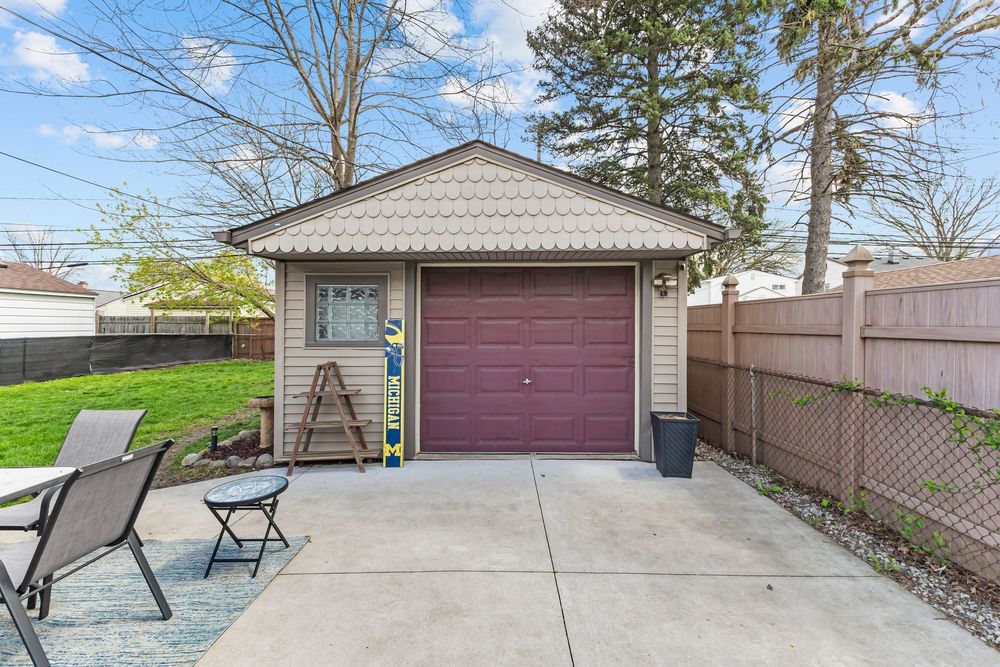 Detached garage with burgundy door, concrete driveway, and wooden privacy fence in backyard.