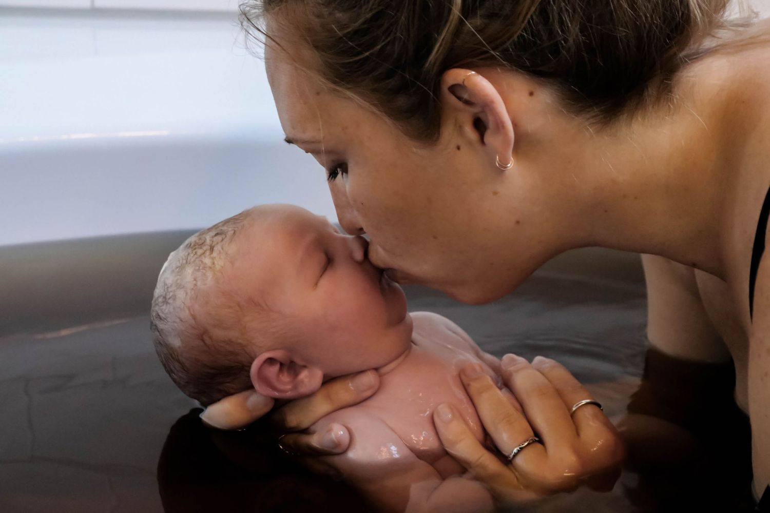 Mother tenderly kissing her newborn baby during a water birth in a birthing tub.