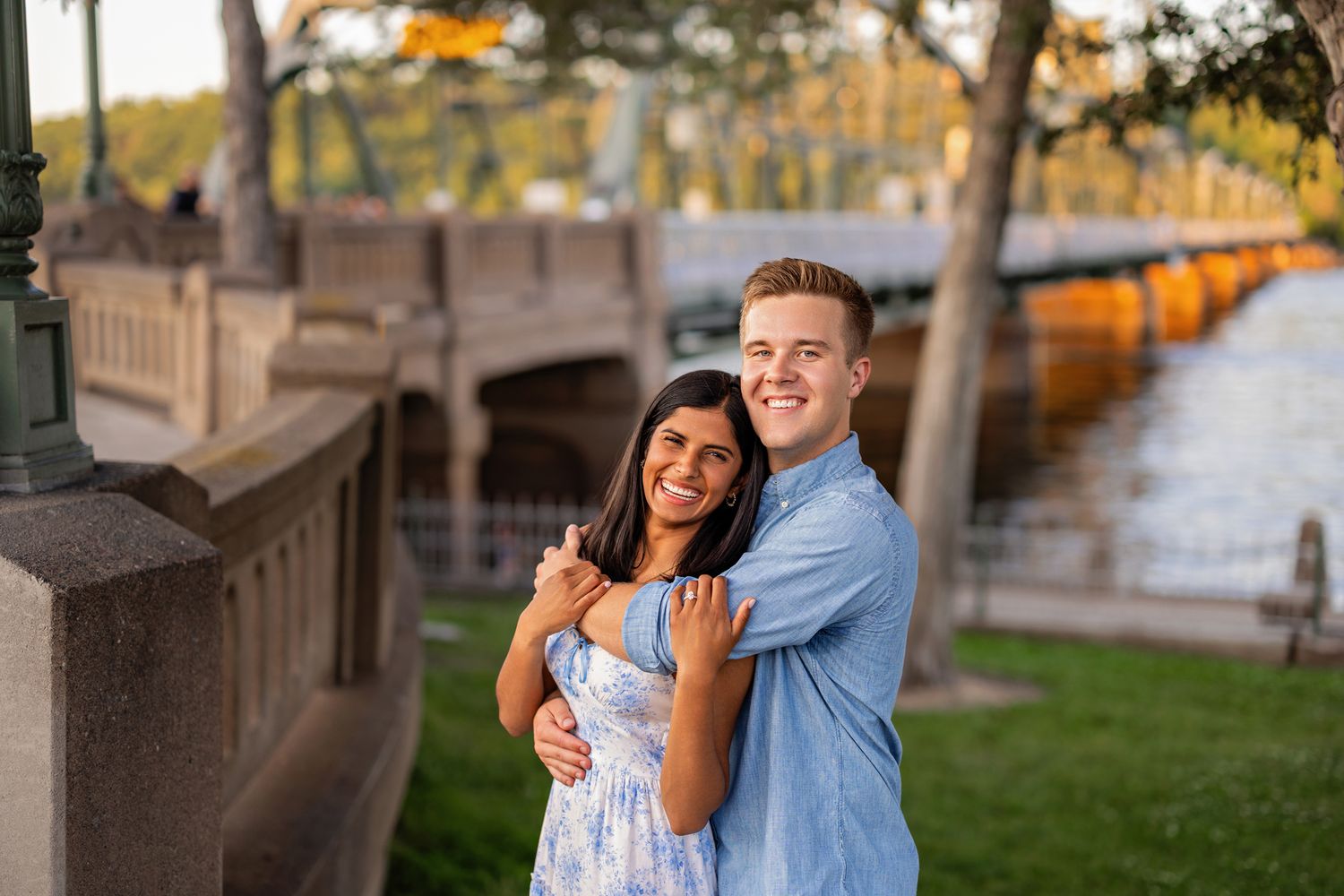 Happy couple embracing near a stone bridge railing in warm golden evening light.