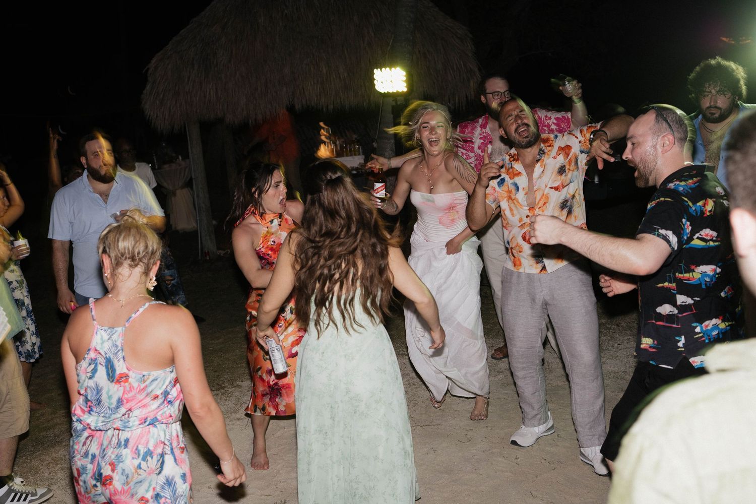 Bride and guests dancing outdoors at a tropical beach wedding reception at night.