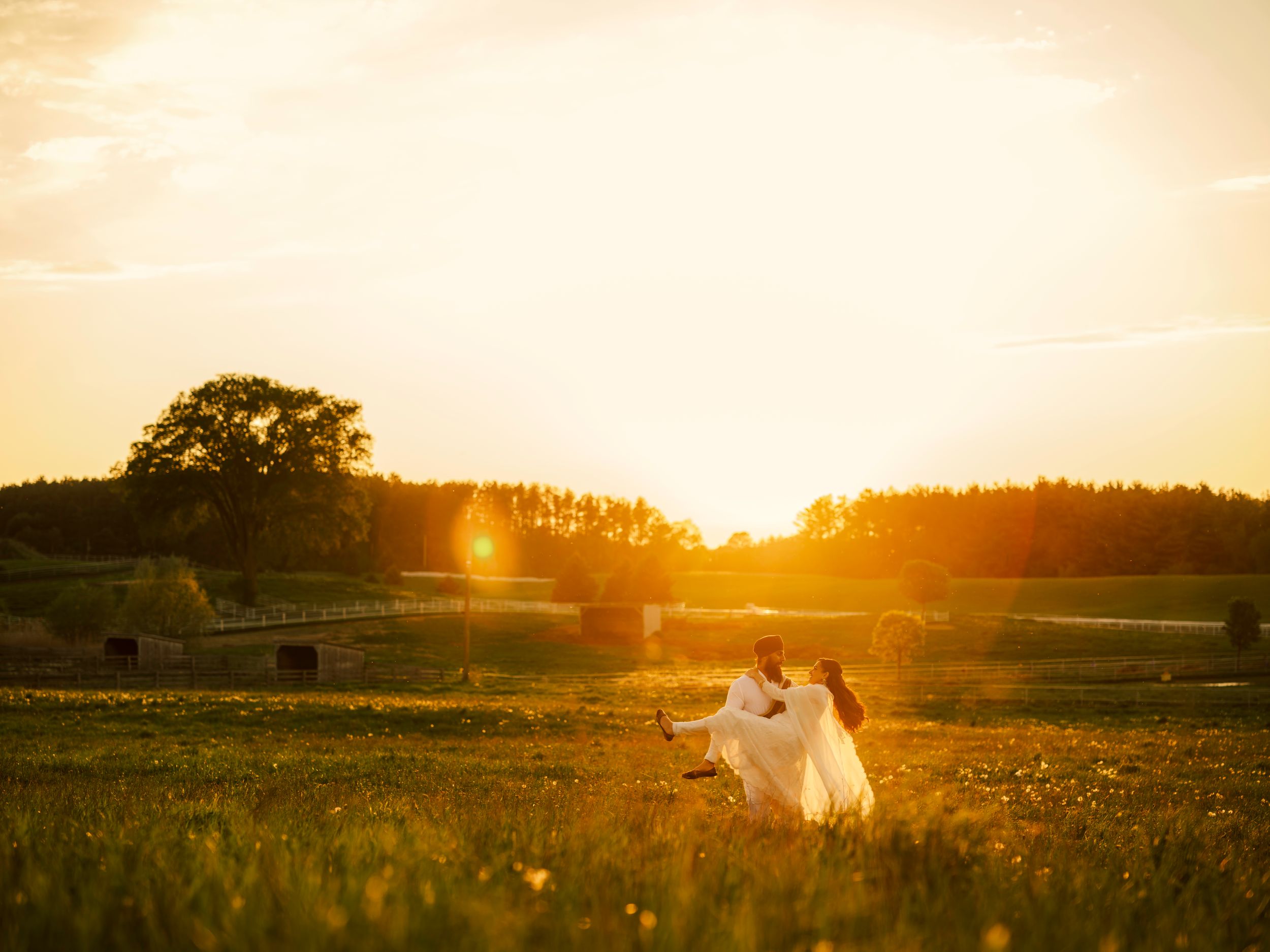 Couple dancing in a sunlit meadow at golden hour, surrounded by lush greenery and warm sunset glow.