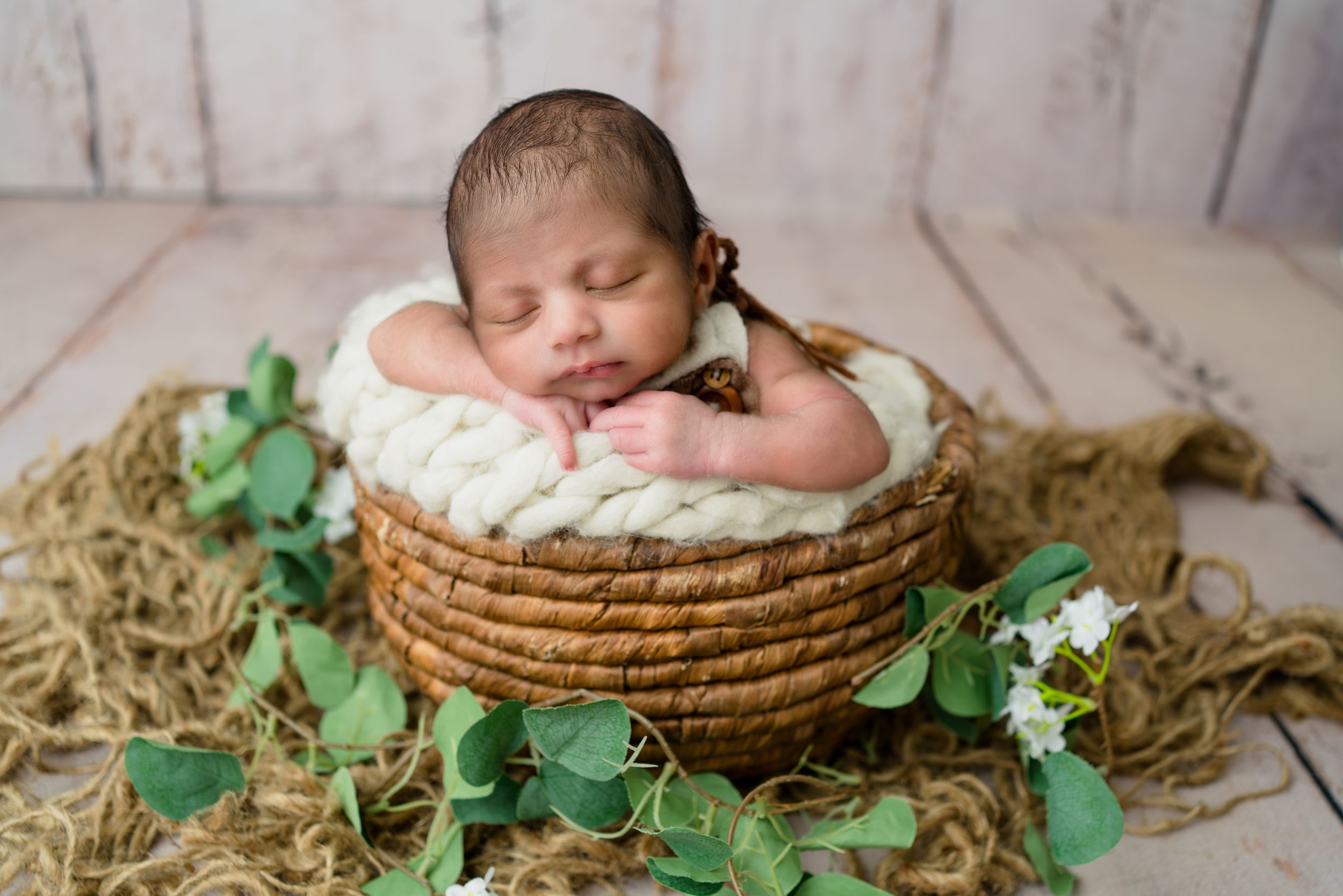 Newborn baby sleeping in basket with green leaves, studio photoshoot