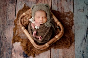 Newborn baby in brown cloth lying in basket, studio photoshoot