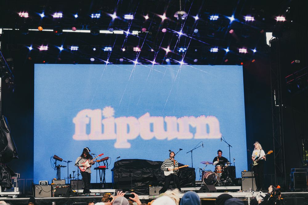 Flipturn band performing live on stage at an outdoor music festival with a blue retro logo backdrop.