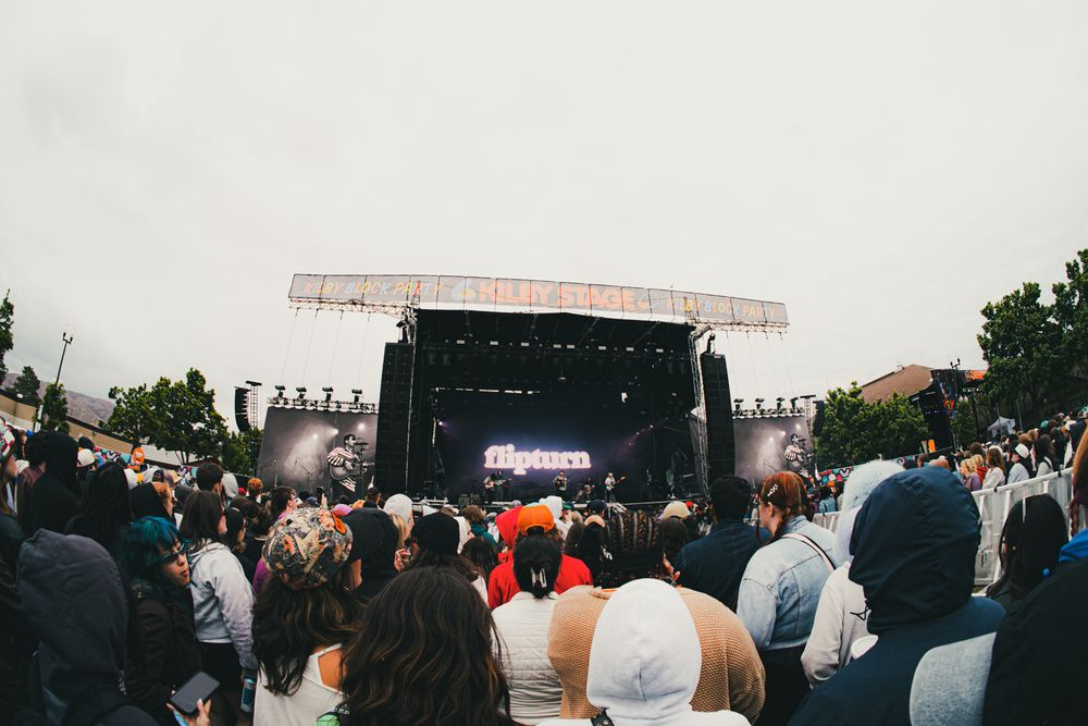 Crowd gathered at an outdoor music festival stage on a cloudy day.