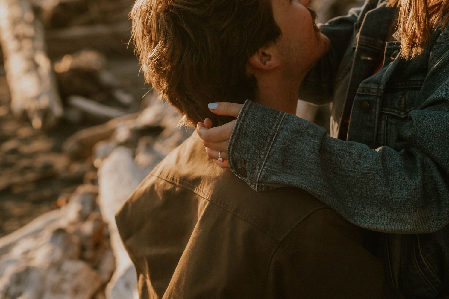 A couple shares a tender romantic moment outdoors, with a woman gently touching a mans hair in warm golden light.