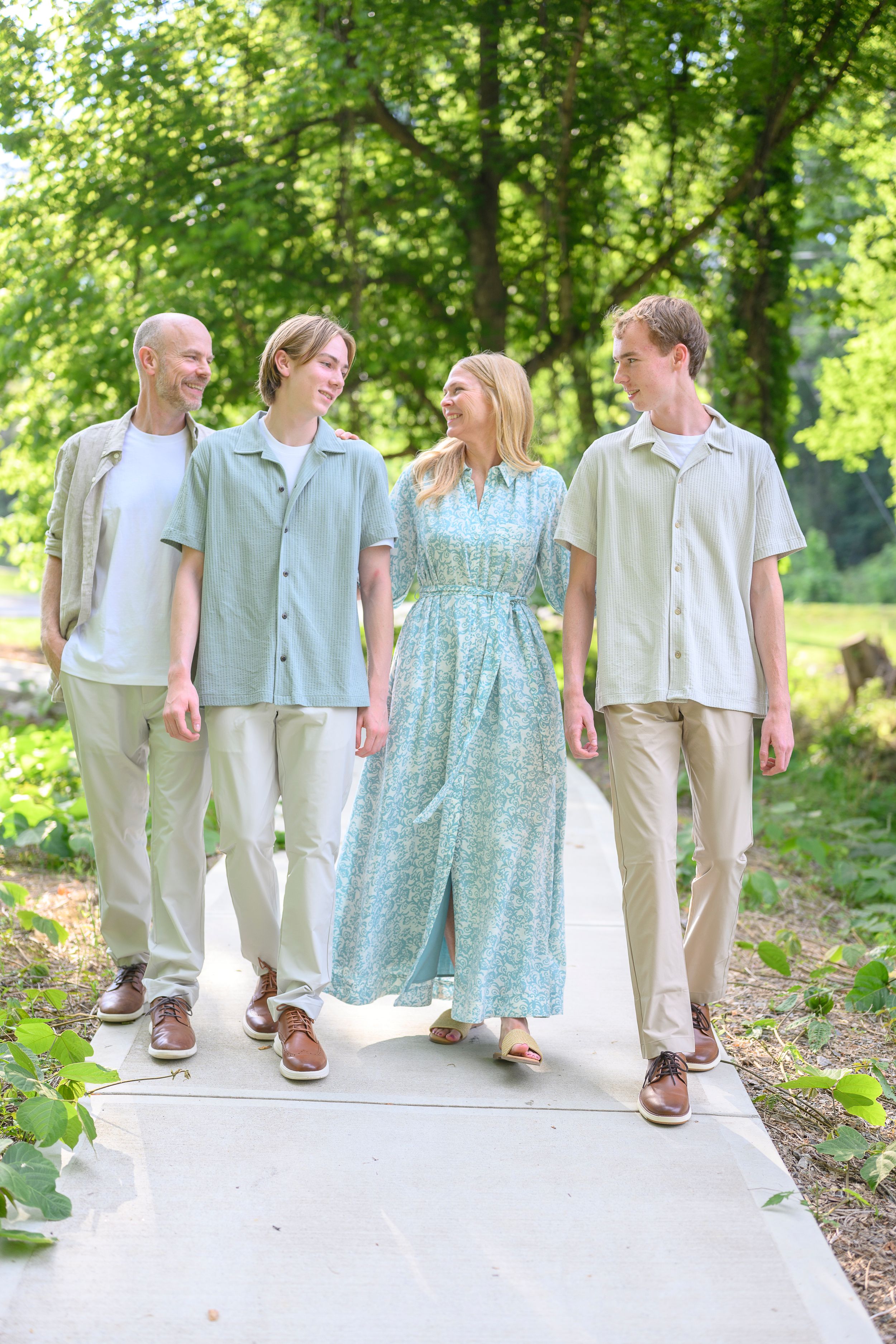 Family of four walking on a path in a lush green park, wearing coordinated sage green and beige outfits.