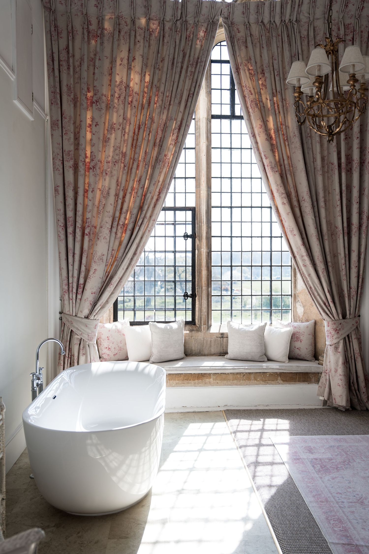 Luxurious bathroom with freestanding white bathtub, draped curtains, and window seat.