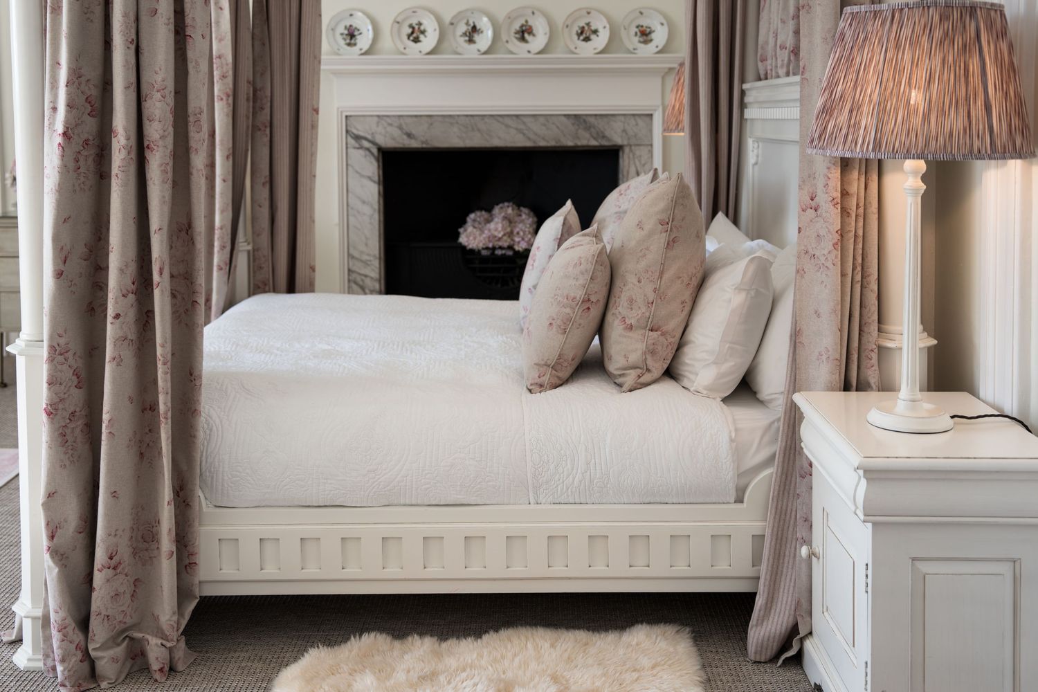 Romantic French-style bedroom with ornate white fireplace and floral curtains.