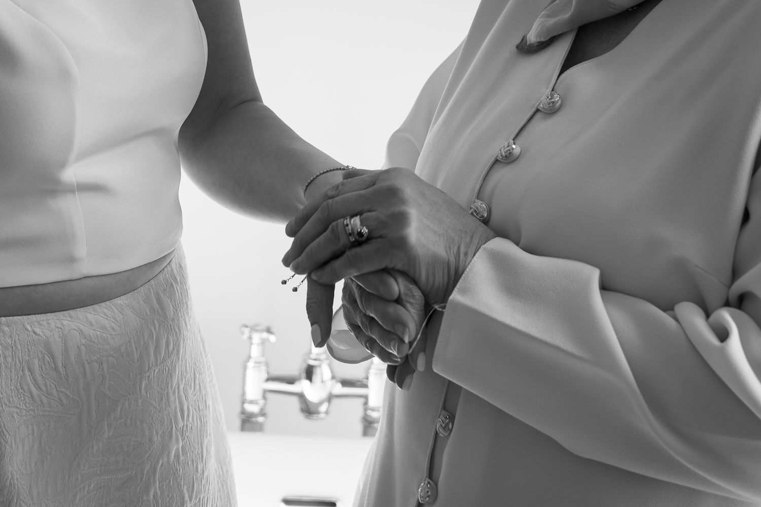 Black and white close-up of bride and older woman holding hands, showing wedding ring detail.