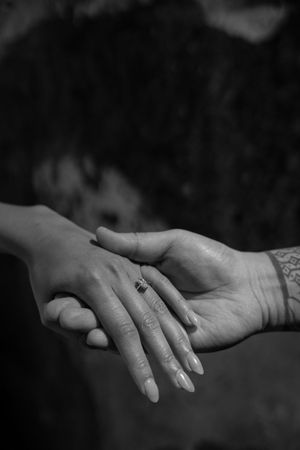 Black and white photo of two hands touching, one with a ring and the other with a tattoo.