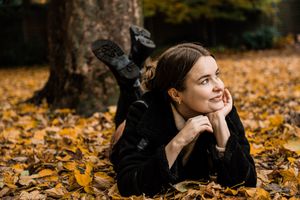 Eine junge Frau im Herbst liegt auf dem Blätterboden und schaut verträumt zur Seite