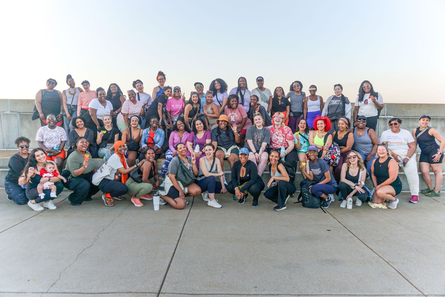 Large diverse group of people posing together outdoors on a rooftop at sunset for a group photo.