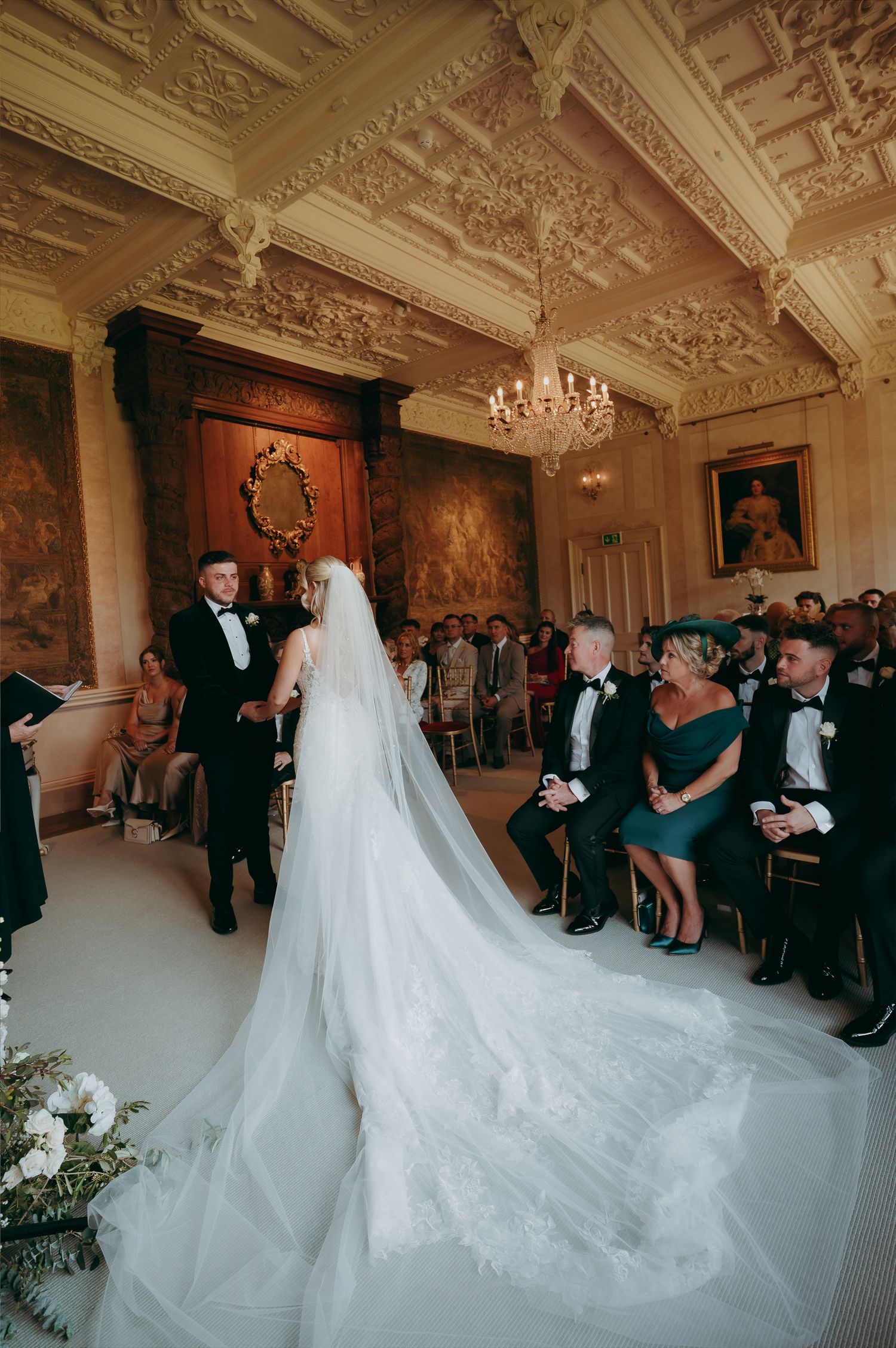 Black and white outdoor wedding ceremony in the rain with guests holding umbrellas under string lights in a wooded setting.