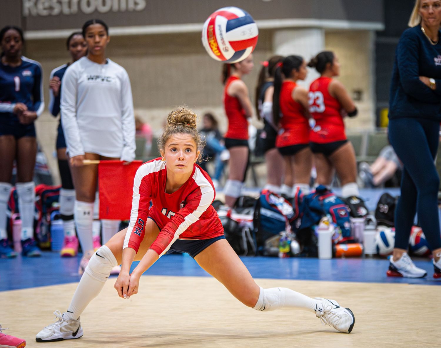 Female volleyball player in red uniform performing a dig during an indoor volleyball match.