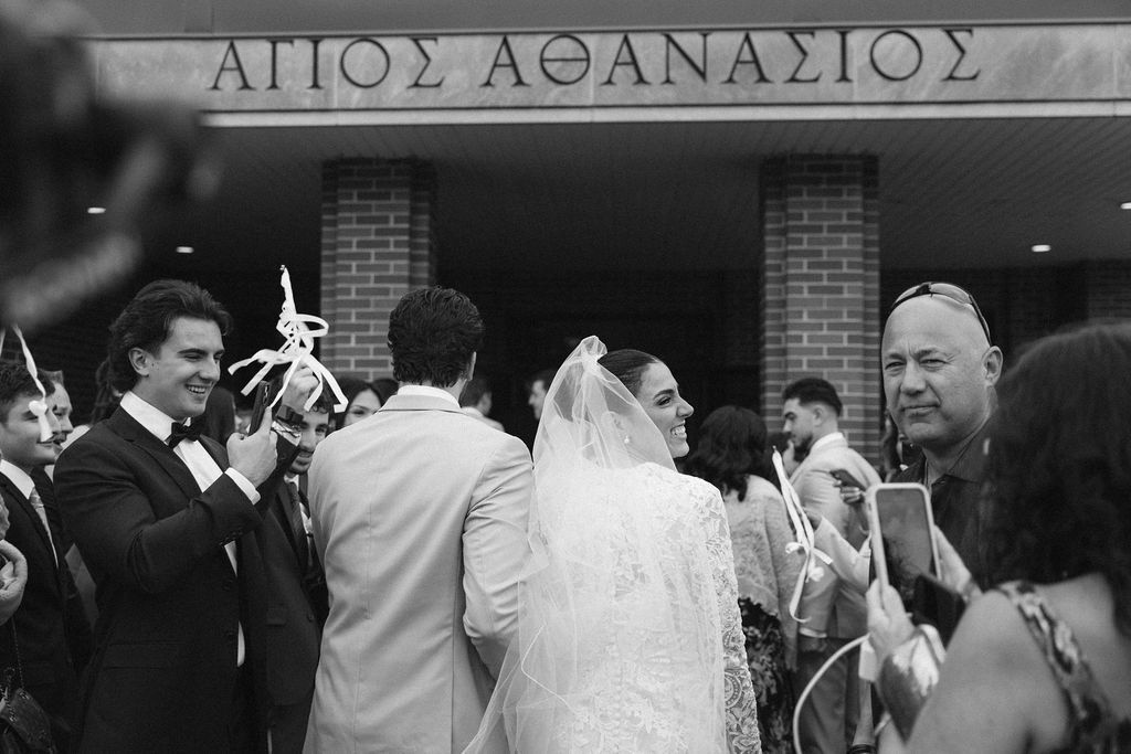 Black and white wedding photo outside Agios Athanasios Greek Chicago Orthodox church with bride in veil and guests celebrating.