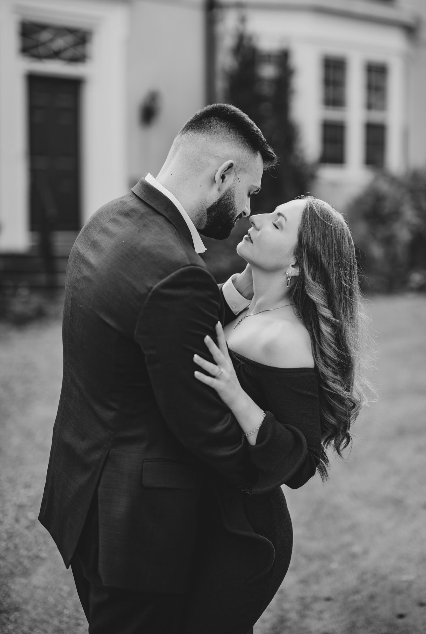Black and white photo of a couple embracing and leaning in for a kiss outside an elegant building.