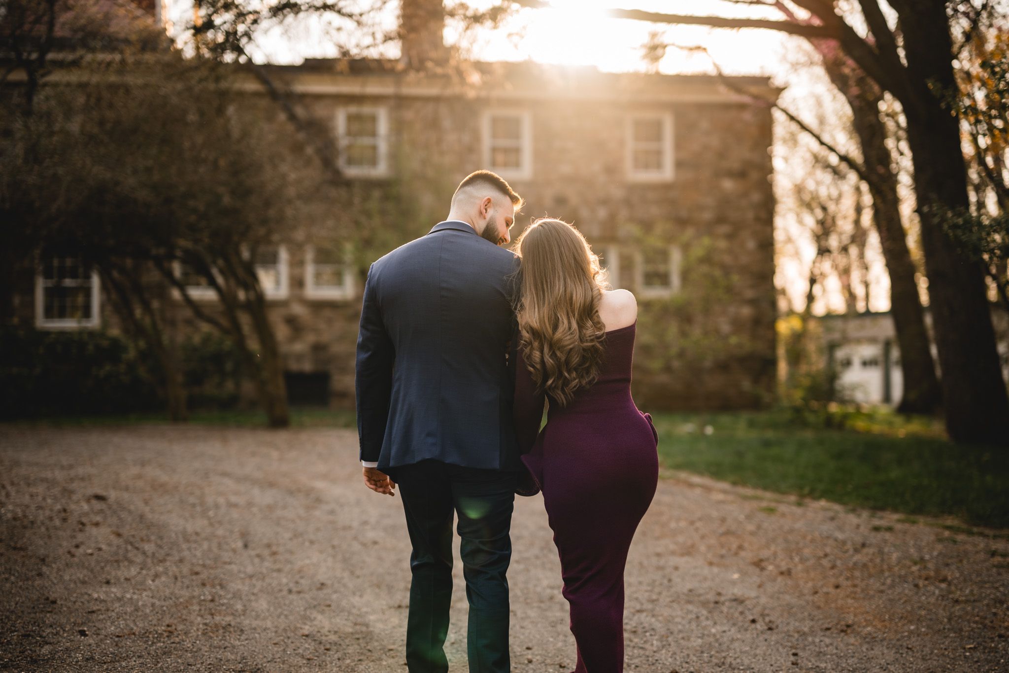 Couple walking hand in hand toward a historic stone house at golden hour sunset.
