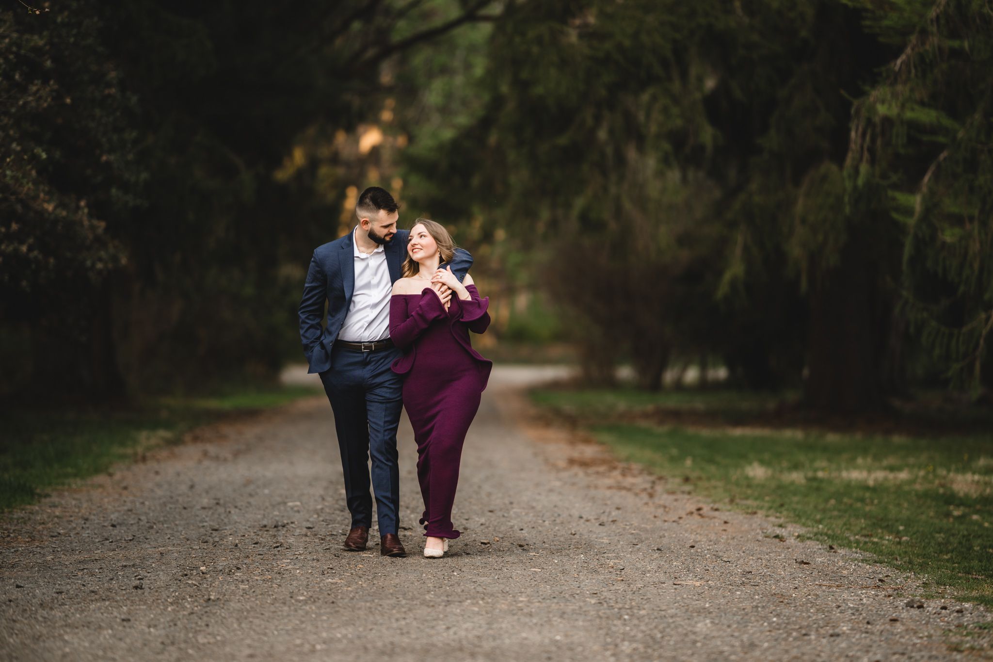 Couple walking arm in arm down a tree-lined path in coordinating formal attire.