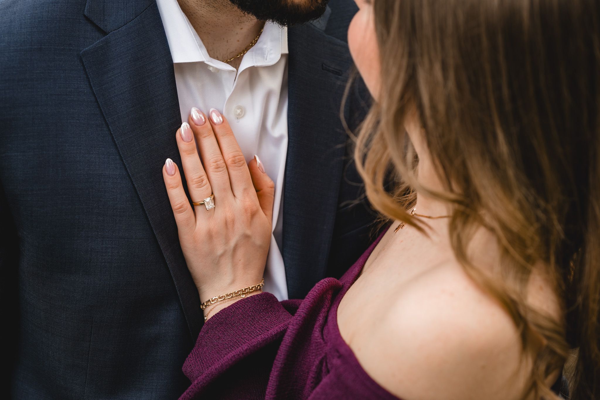 Close-up of woman's hand with engagement ring resting on man's chest in navy suit, romantic couple moment.
