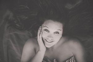 Black and white portrait of a smiling young woman lying down, hand on cheek, with flowing hair spread around her.