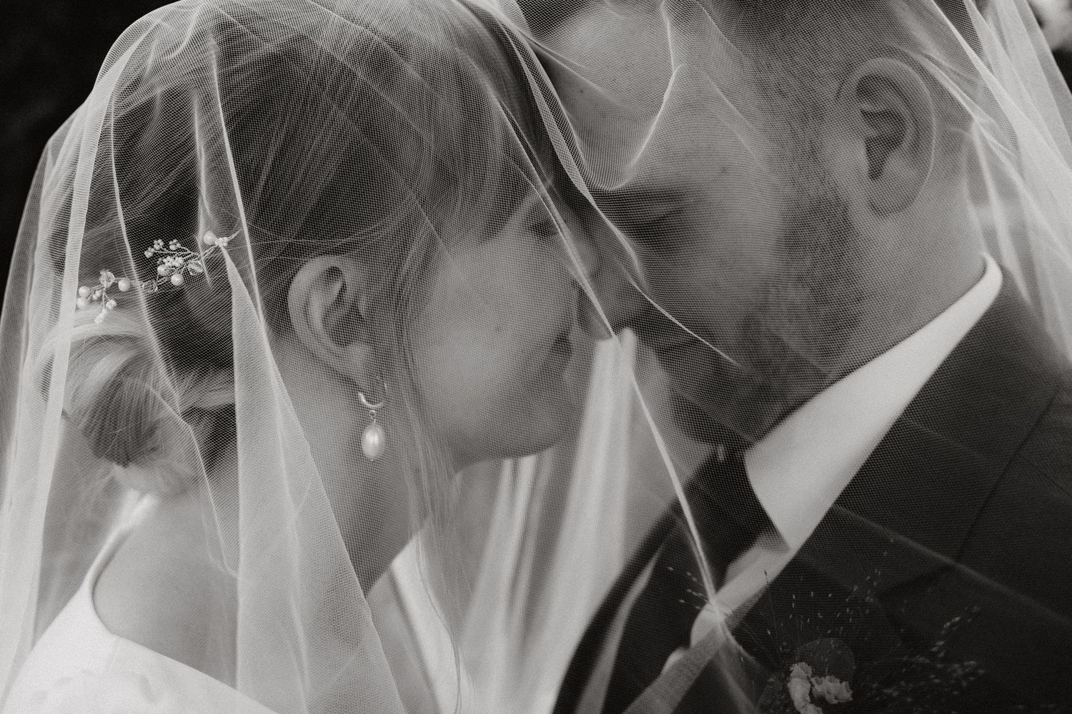 Black and white photo of bride and groom sharing an intimate moment under a wedding veil.