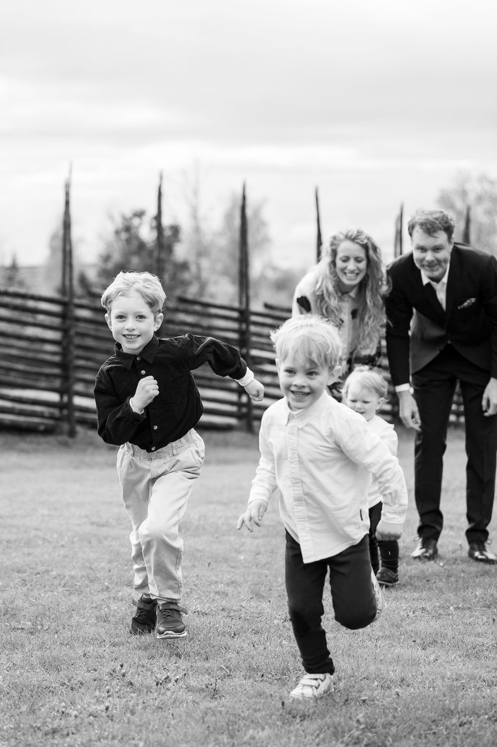 Two young boys running and laughing outdoors during a family photo session in black and white.