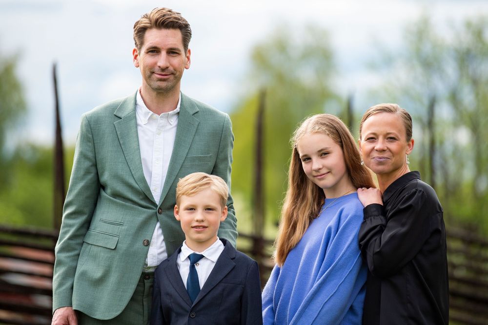 Family of four posing outdoors, father in green blazer, son in suit, teenage daughter, and mother smiling together.