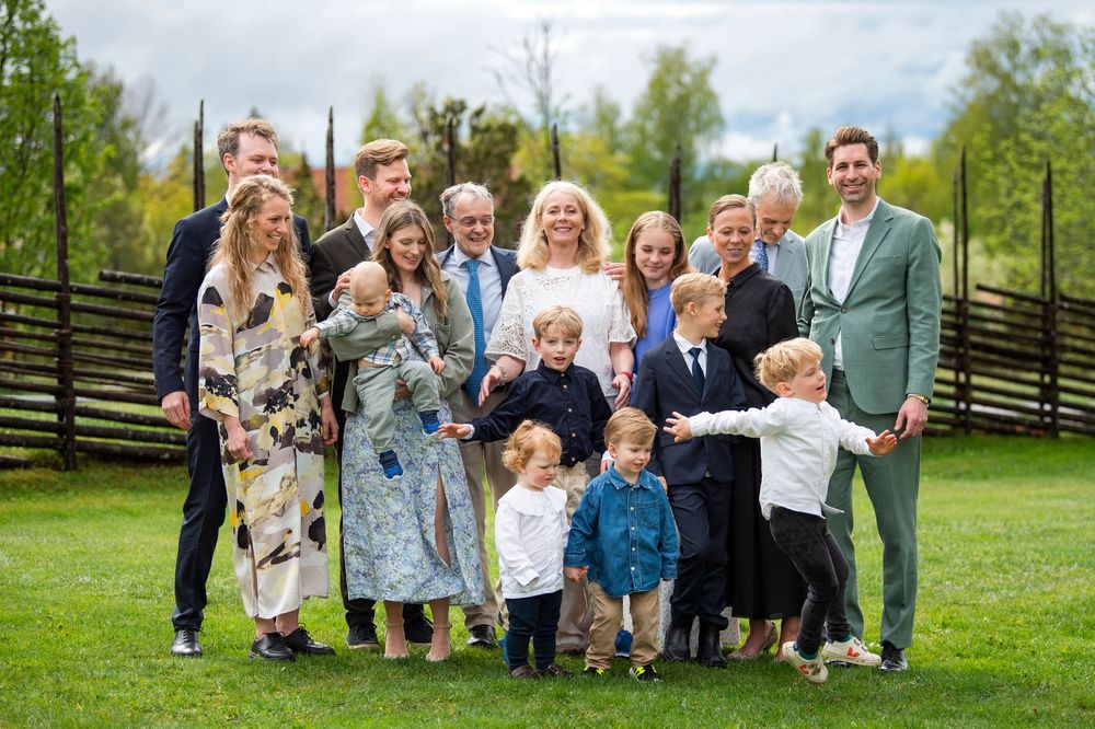 Large family group photo outdoors on green grass, adults and children smiling together at a festive celebration.