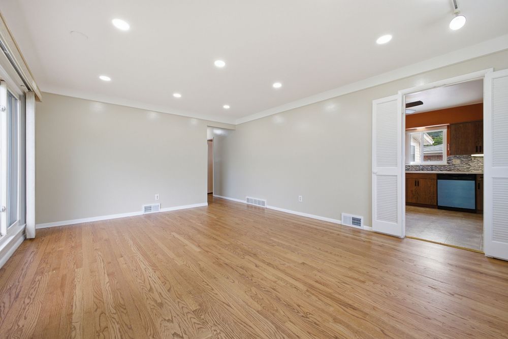 Bright empty living room with hardwood floors, recessed lighting, crown molding, and open view to kitchen.
