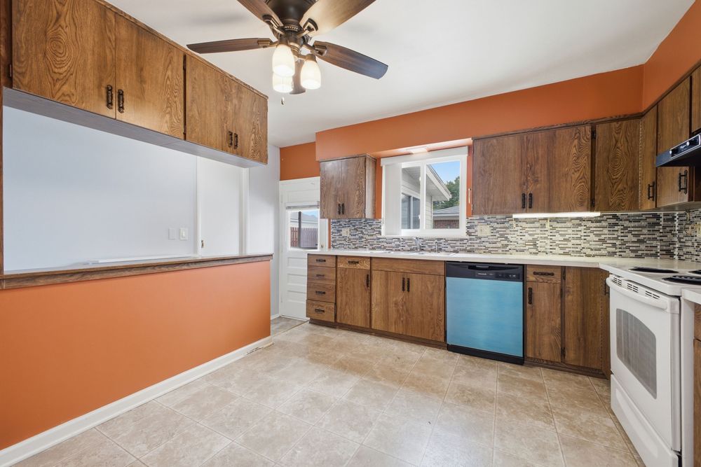 Kitchen with brown wood cabinets, white electric range, blue dishwasher, mosaic tile backsplash, and orange accent walls.