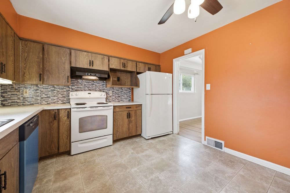 Kitchen with orange walls, brown cabinets, white appliances, tile backsplash, and light tile flooring.