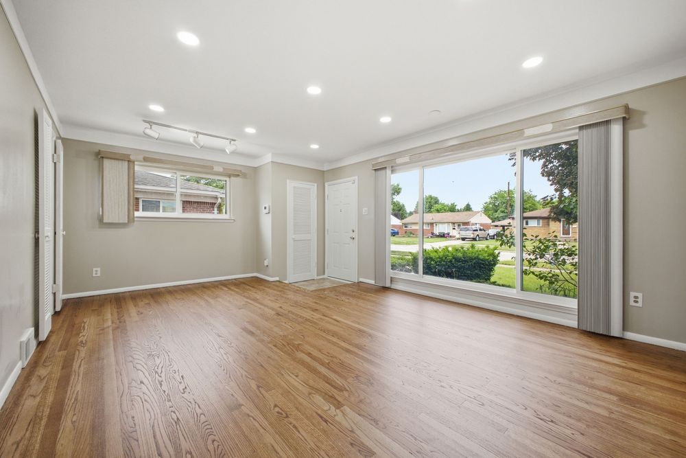 Bright empty living room with hardwood floors, recessed lighting, crown molding, and large sliding glass door overlooking a green yard.