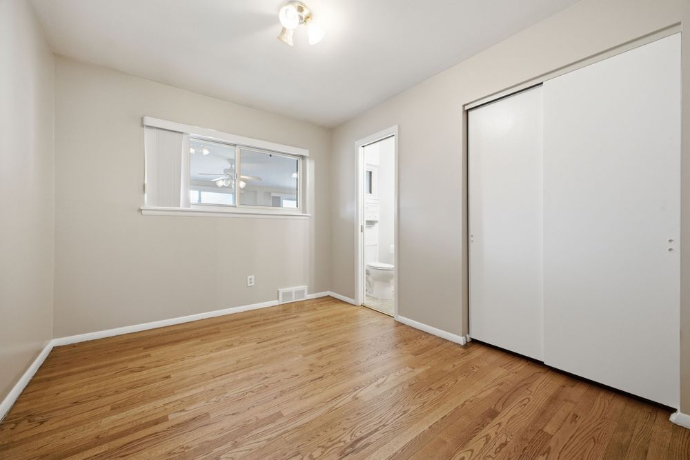 Bright empty bedroom with hardwood floors, closet, and window allowing natural light.