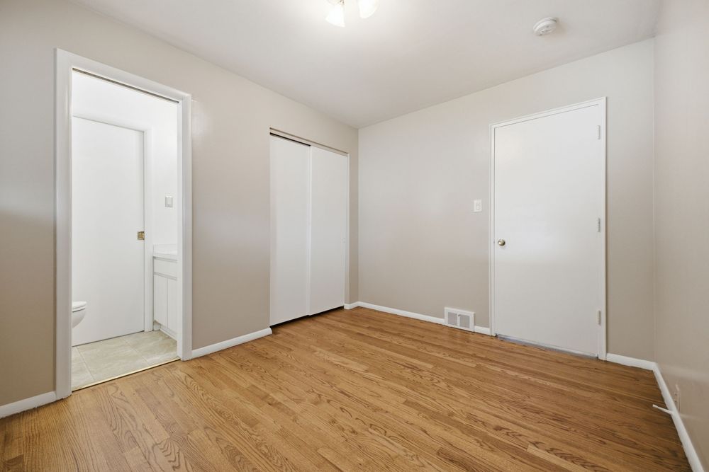 Bright bedroom with hardwood floors, closet, and en-suite bathroom access in a clean, neutral-toned apartment.