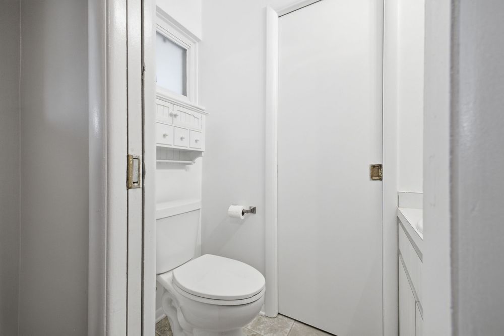 Small white bathroom with a toilet, built-in shelving above, and a white door in a compact, clean space.