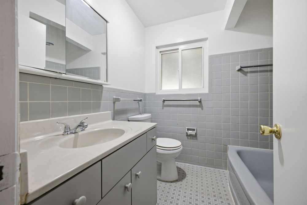 Gray-tiled bathroom with white vanity, mirror cabinet, toilet, and bathtub on mosaic tile floor.