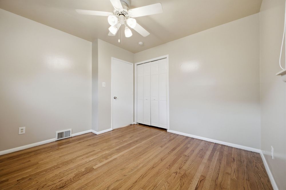 Empty bedroom with hardwood floors, white walls, ceiling fan, and a closet with white doors.