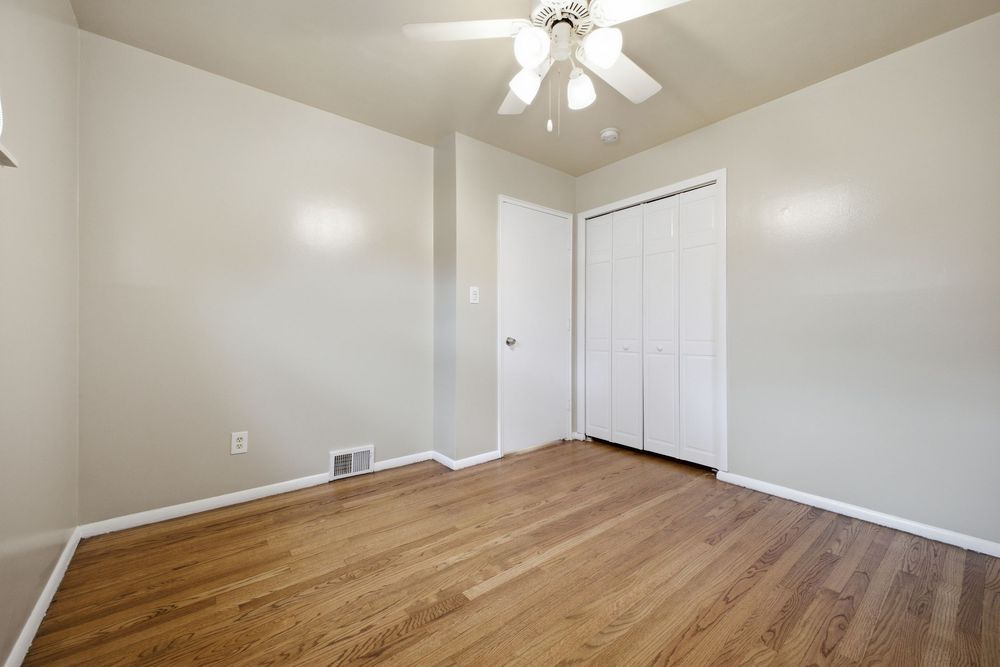 Empty bedroom with hardwood floors, white walls, ceiling fan, and a closet with bifold doors.