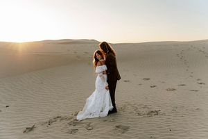 Bride and groom embrace on golden sand dunes during a romantic desert elopement at sunset.