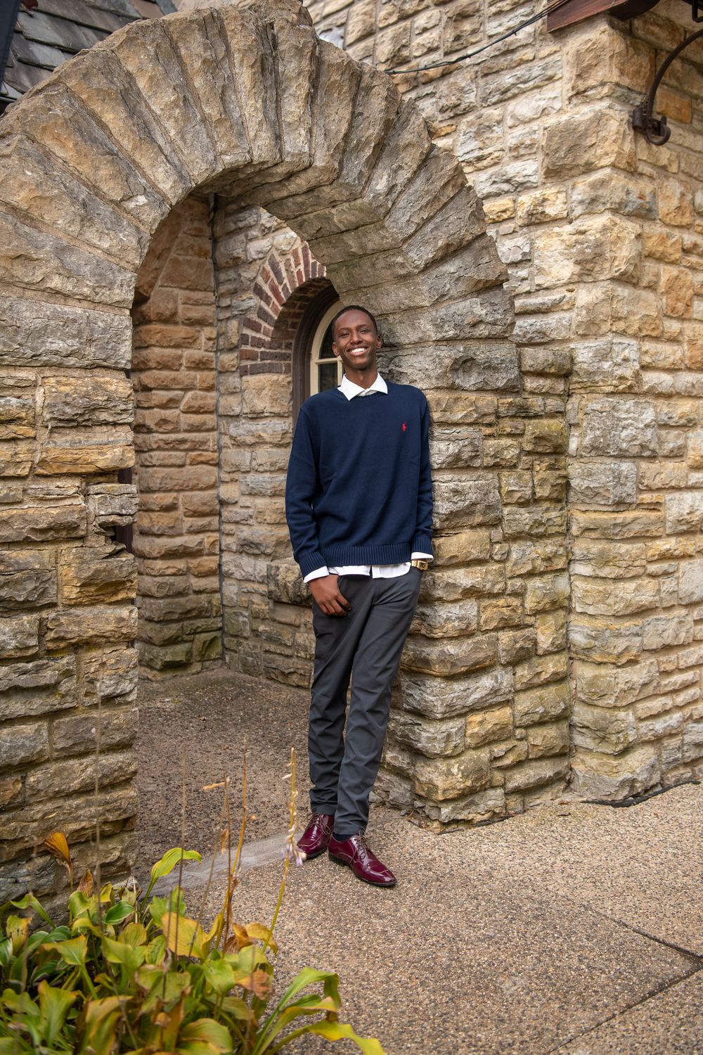 Young man in navy sweater smiling beside a stone archway.