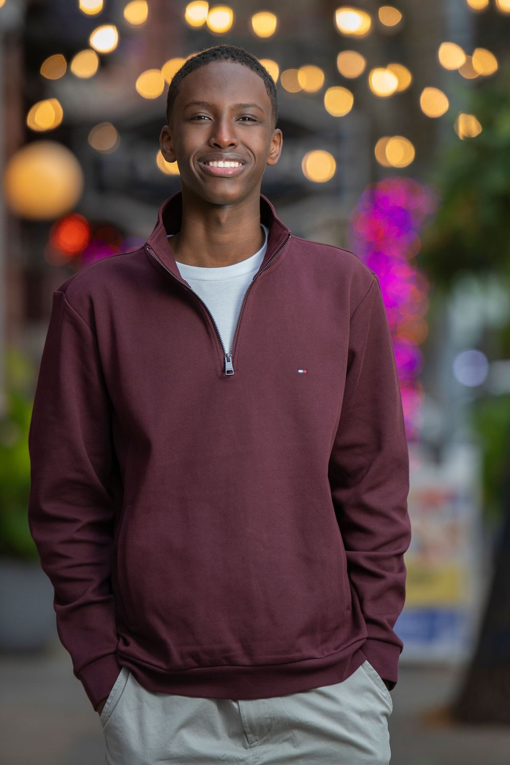 Smiling young man in maroon quarter-zip sweatshirt outdoors at night.